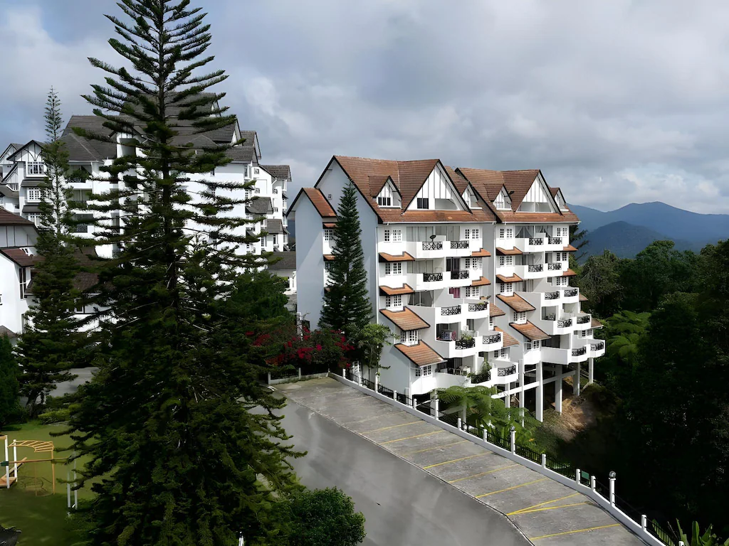 White Tudor-style apartments beside tall pine trees.