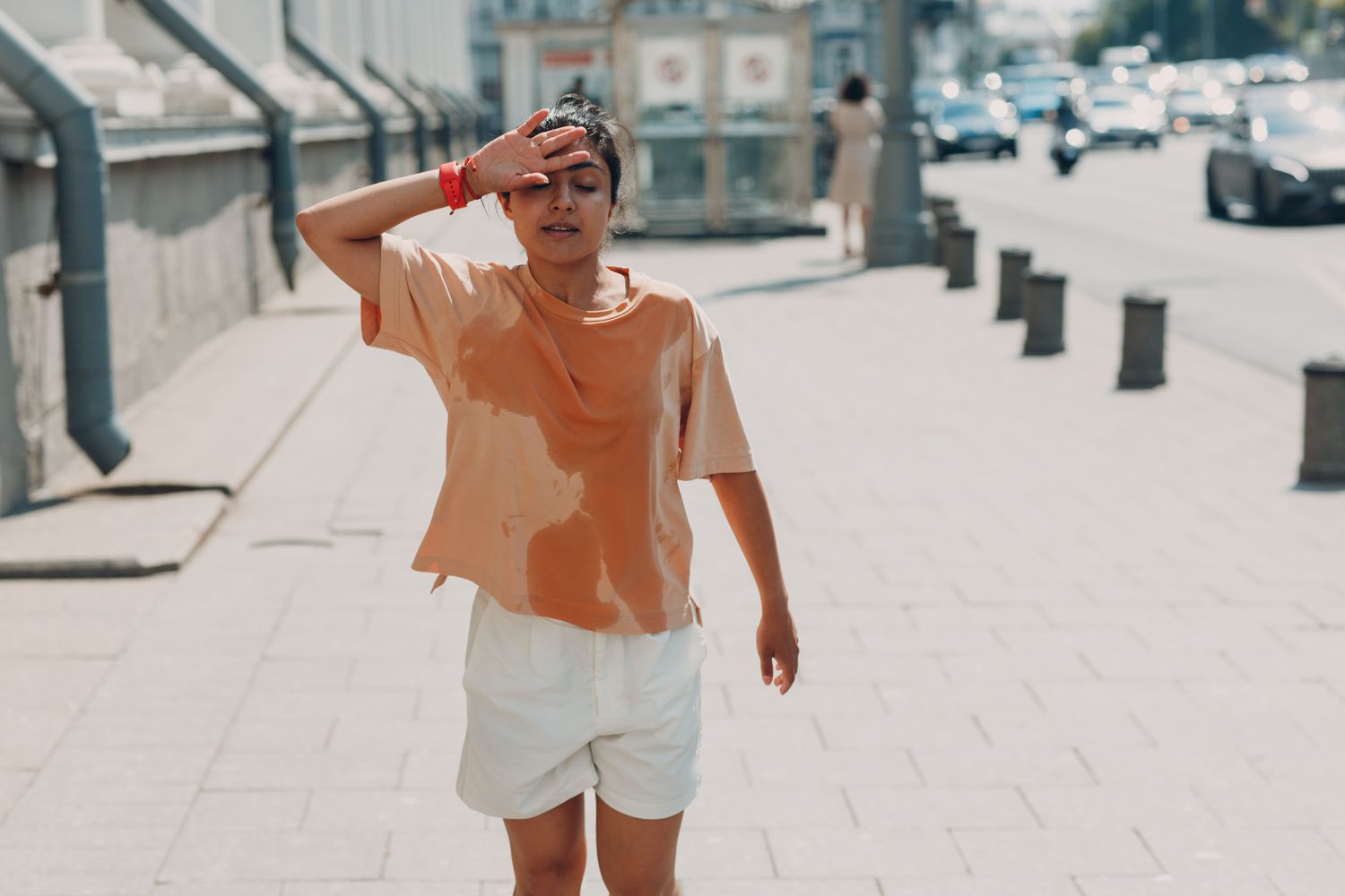 Sweaty woman wiping her forehead in hot weather outdoors.